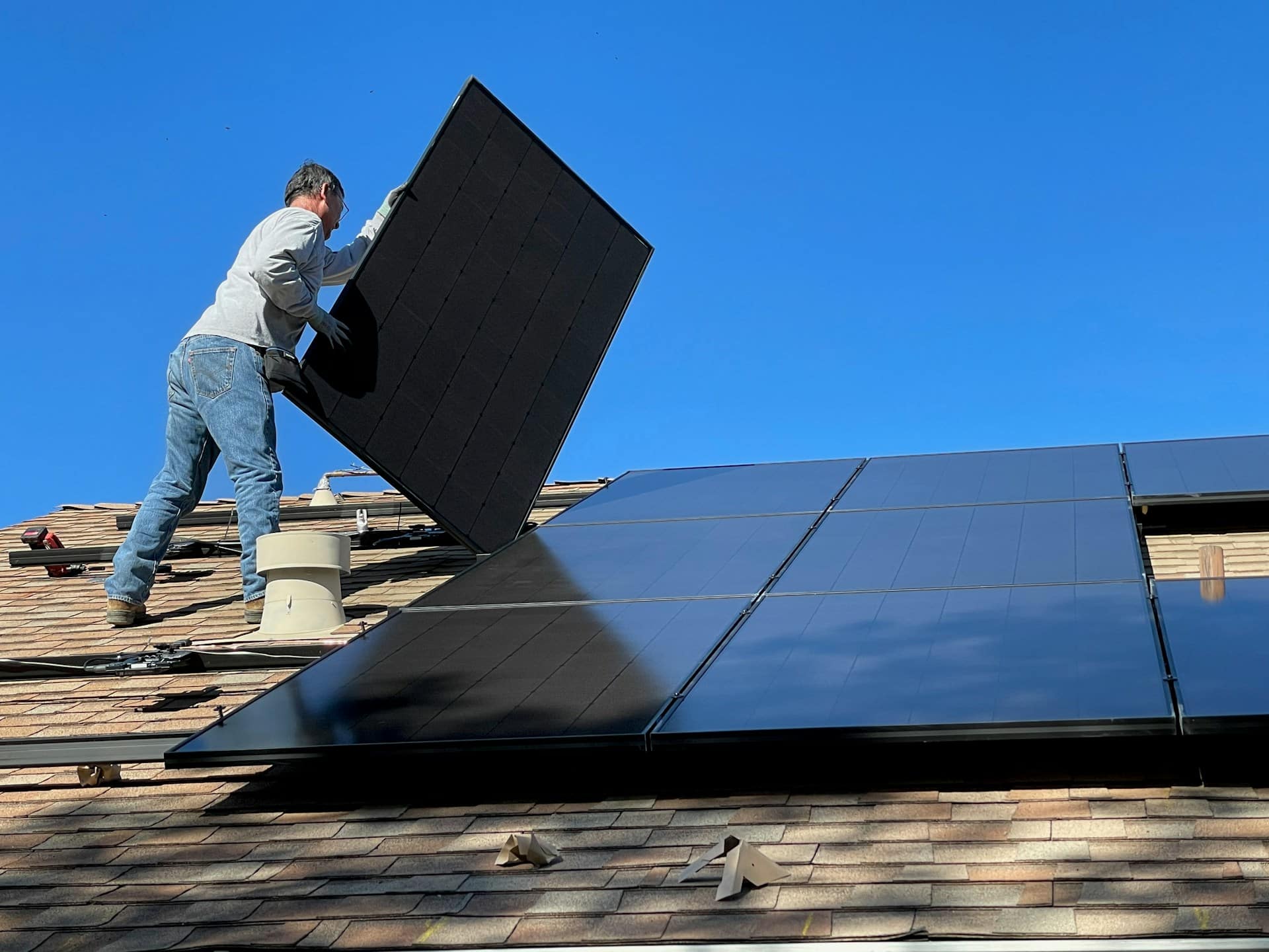 Un artisan installe des panneaux solaires sur le toit d'une maison individuelle.
